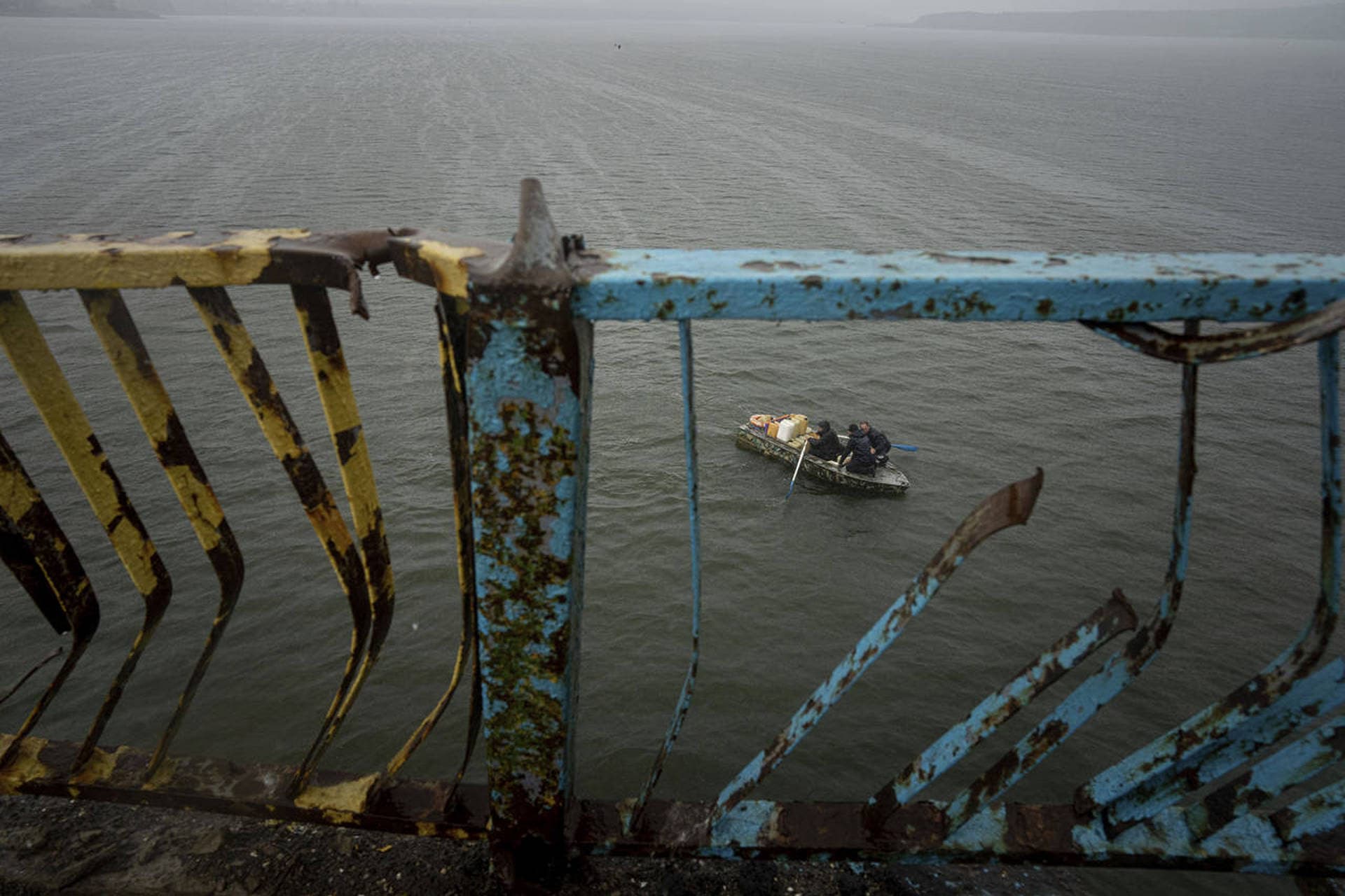 People transport fuel on a boat in front of a destroyed bridge across the Siverskyi-Donets river in Staryi-Saltiv