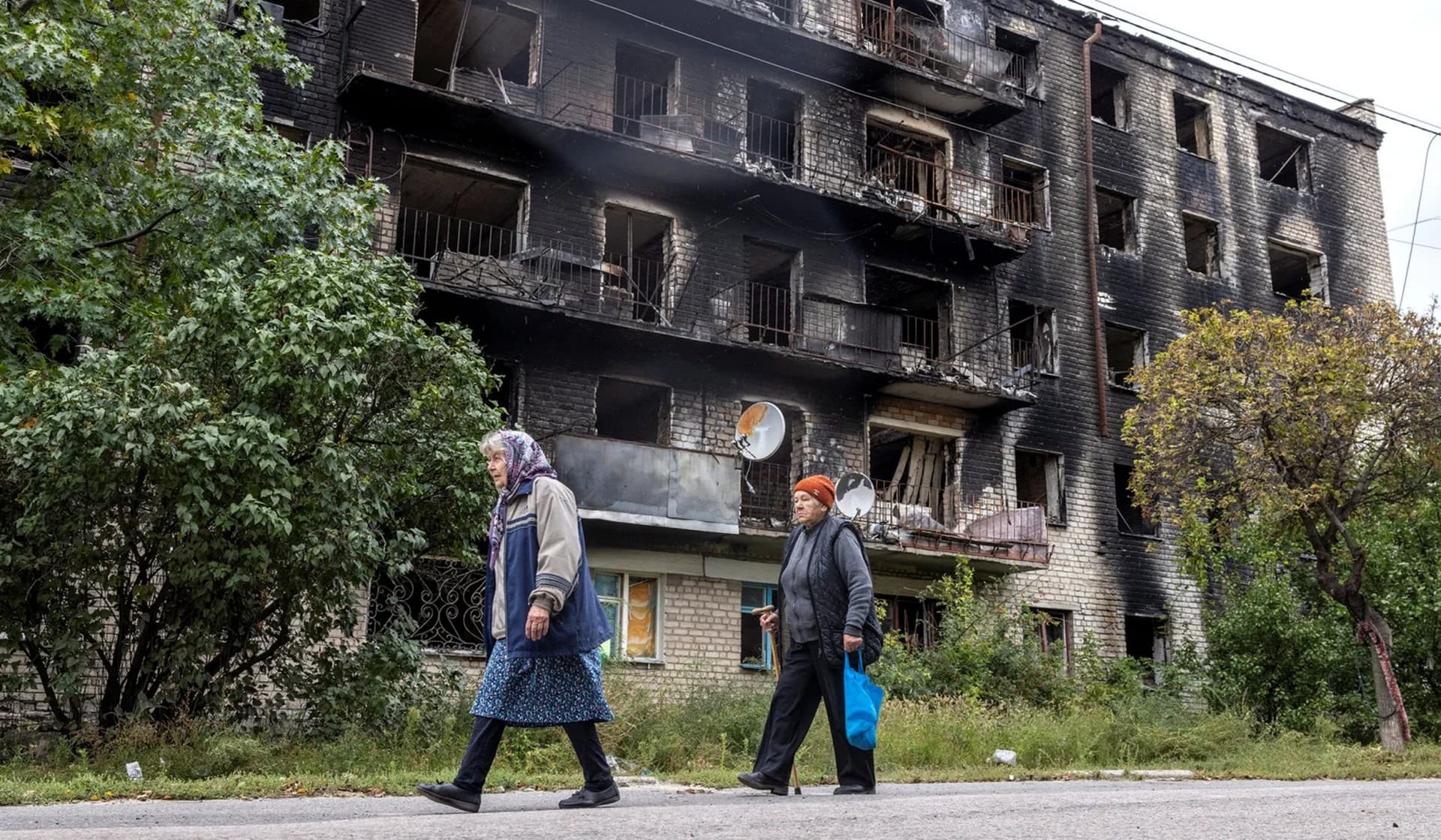 Women walk past a destroyed building in the town of Izium