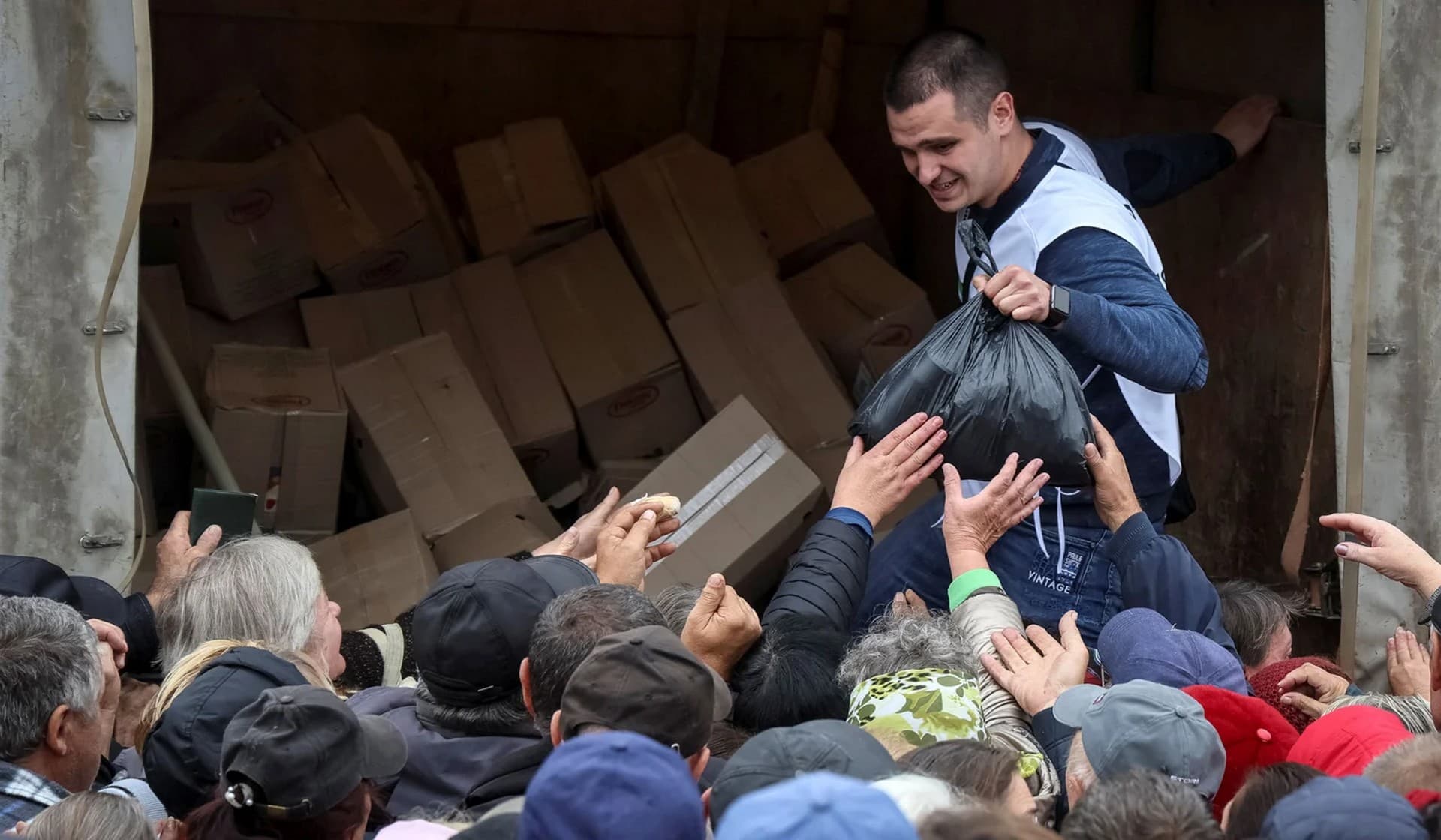 Local residents crowd near a car distributing humanitarian aid in the town of Balakliia