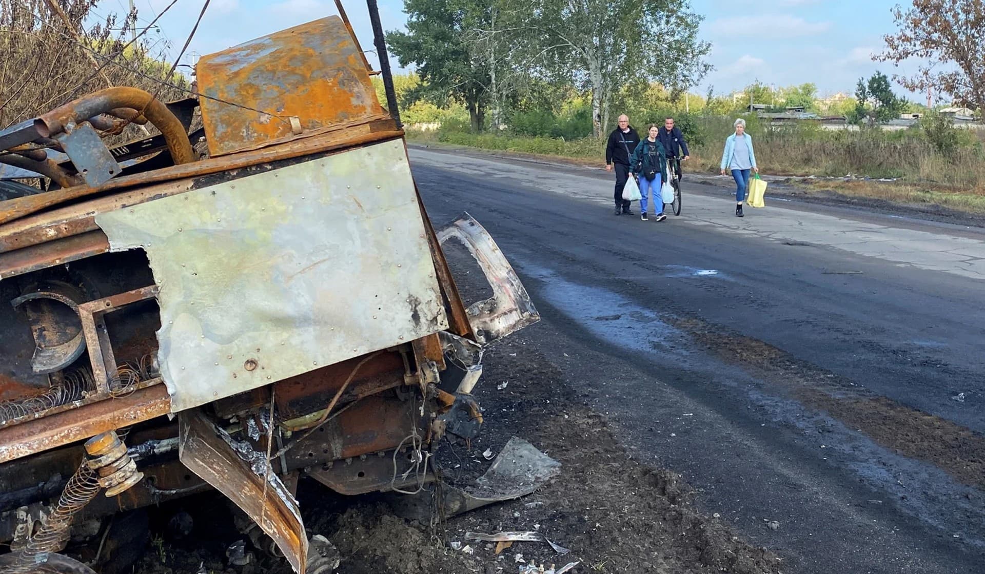 Nataliia Yelistratova with her husband Mykhailio and daughter Olena Miroshnychenko walk along a street past a destroyed military vehicle in their hometown of Balakliia