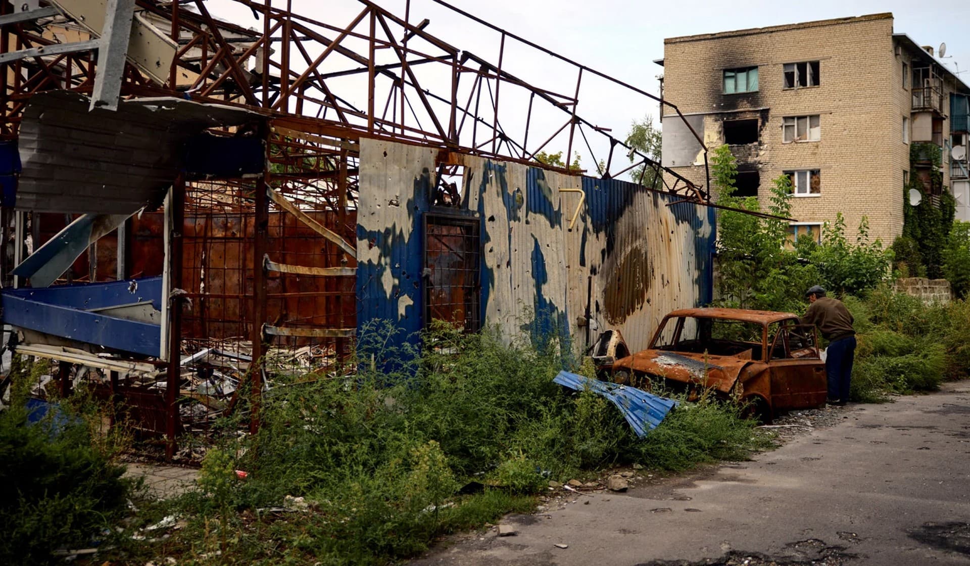 A local resident checks a burned car near a building damaged by military strike in the town of Izium