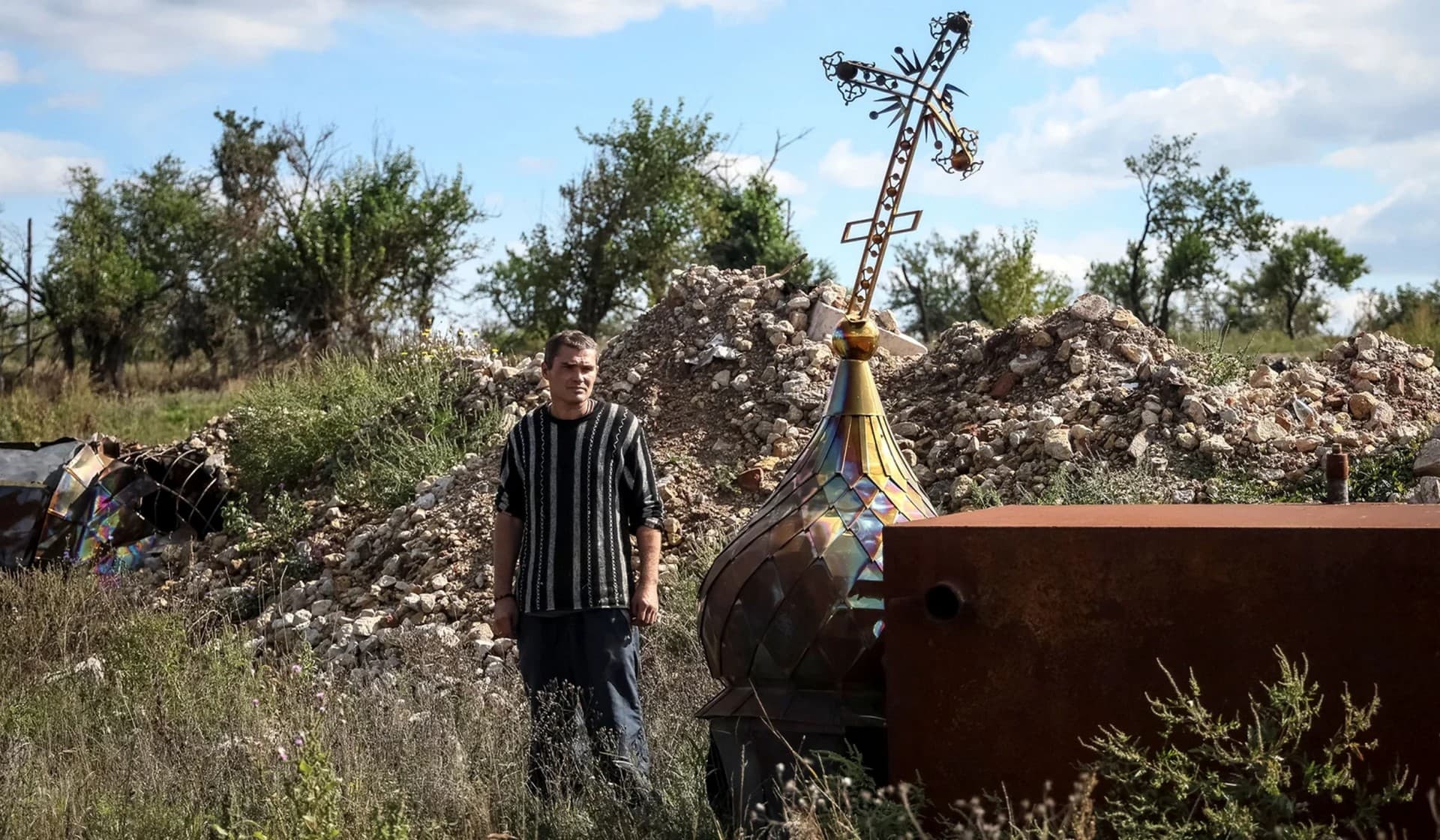 Local resident looks at a cross from a destroyed church in the village of Kamyanka