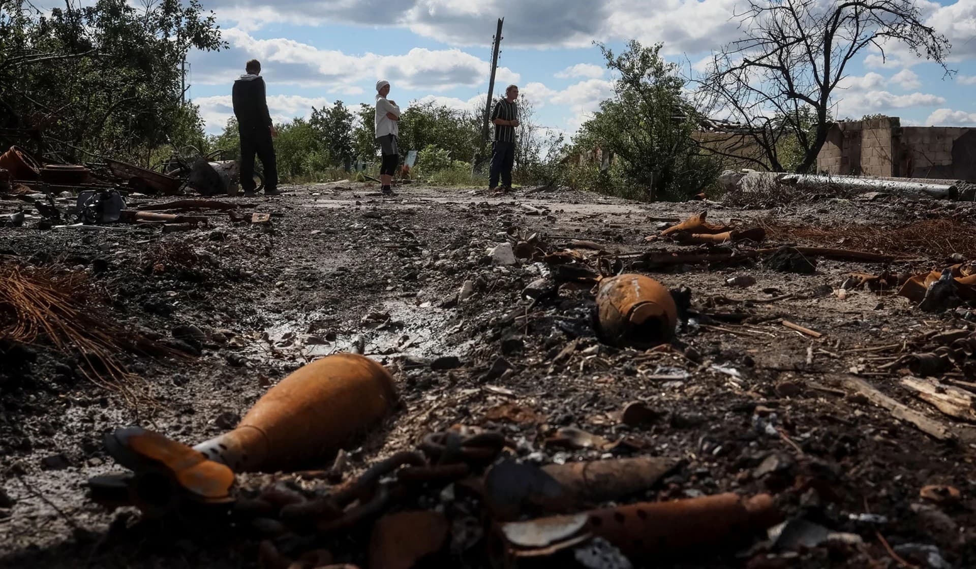 Local residents stand at a destroyed street in the village of Kamyanka
