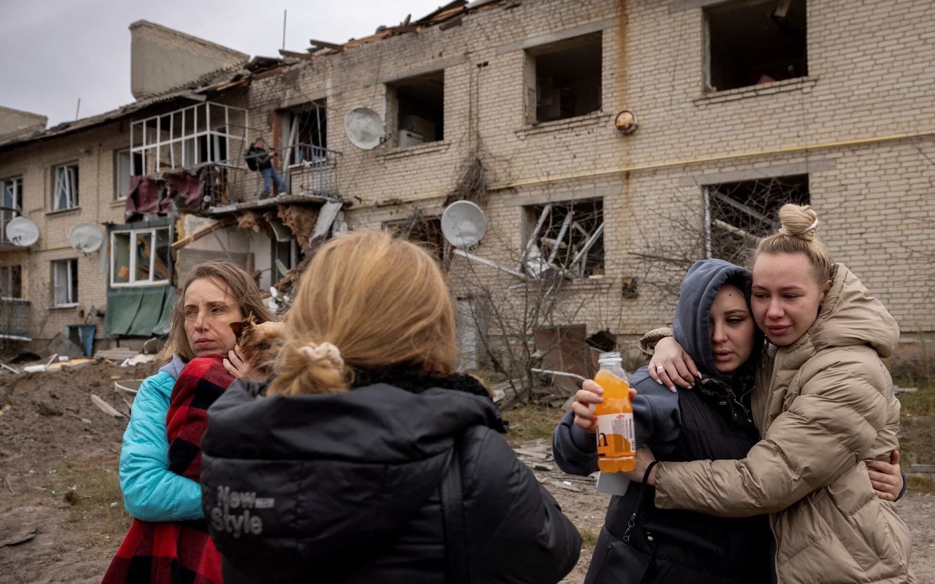 Locals react as they stand at the impact crater of a Russian S-300 missile that hit next to building in Peresichne
