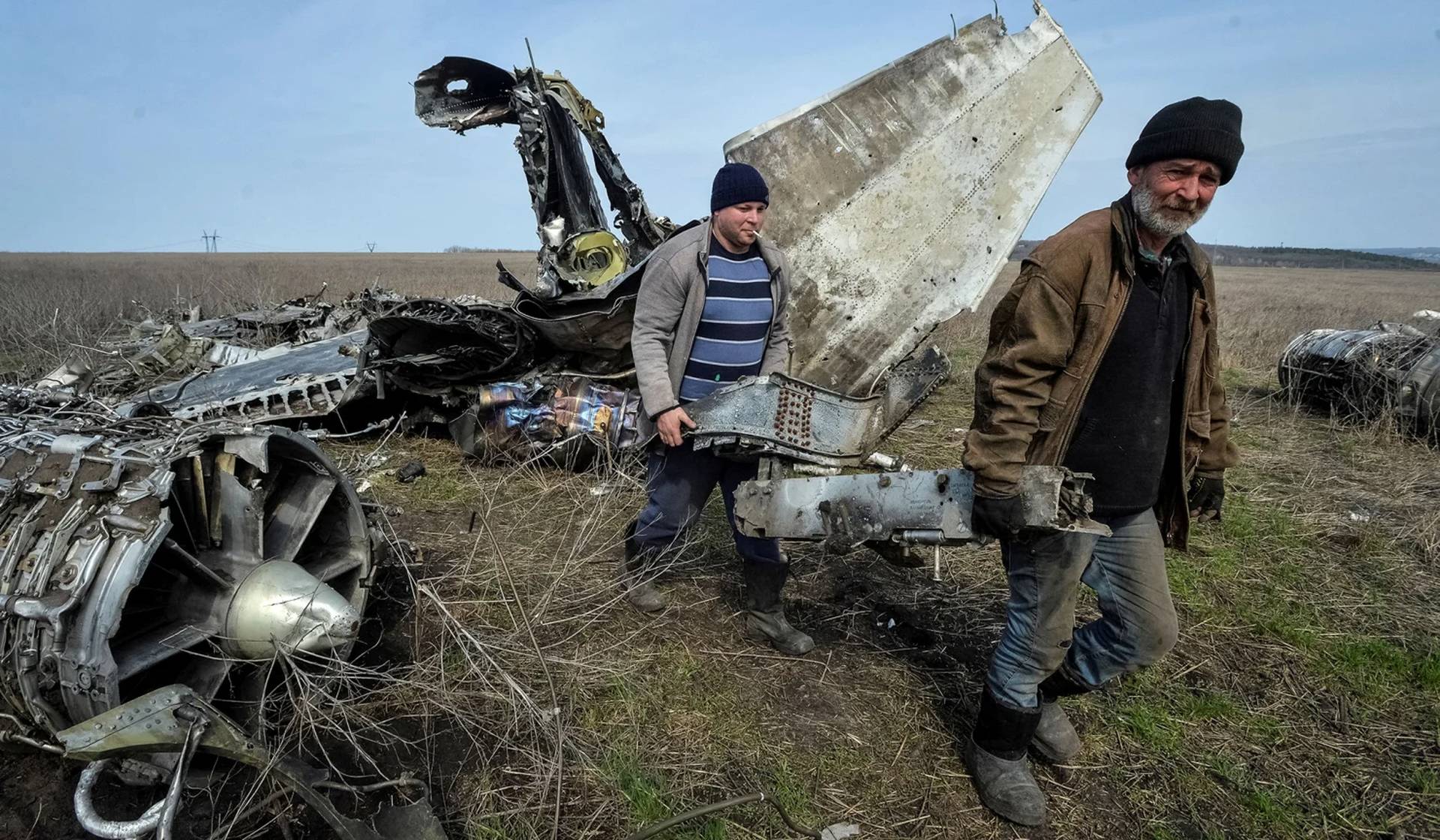 Local residents carry collected scrap metal near a destroyed military plane in Kharkiv Region