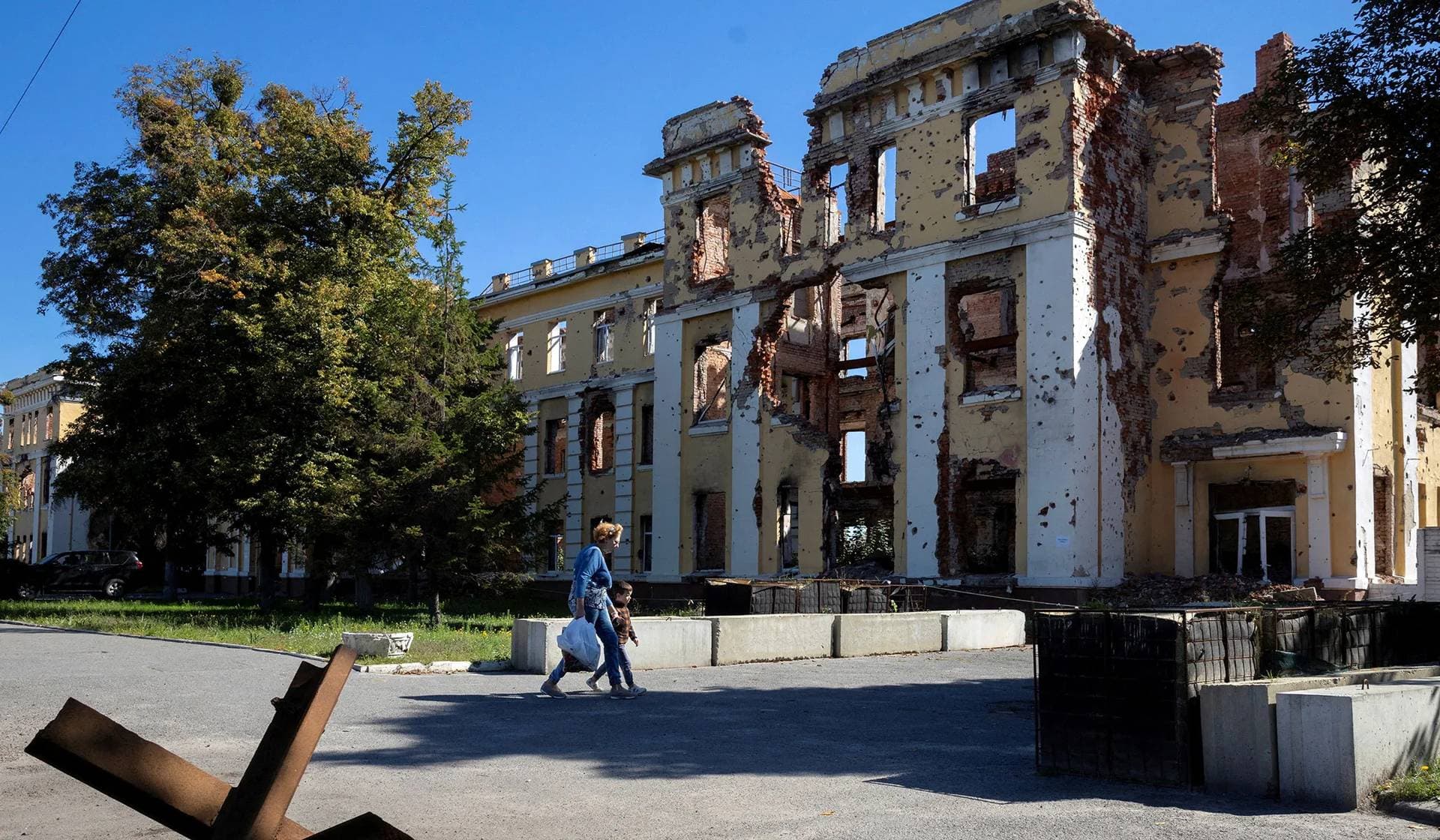 A woman and a child walk past the former German school that was destroyed during fighting with Russian troops in Kharkiv