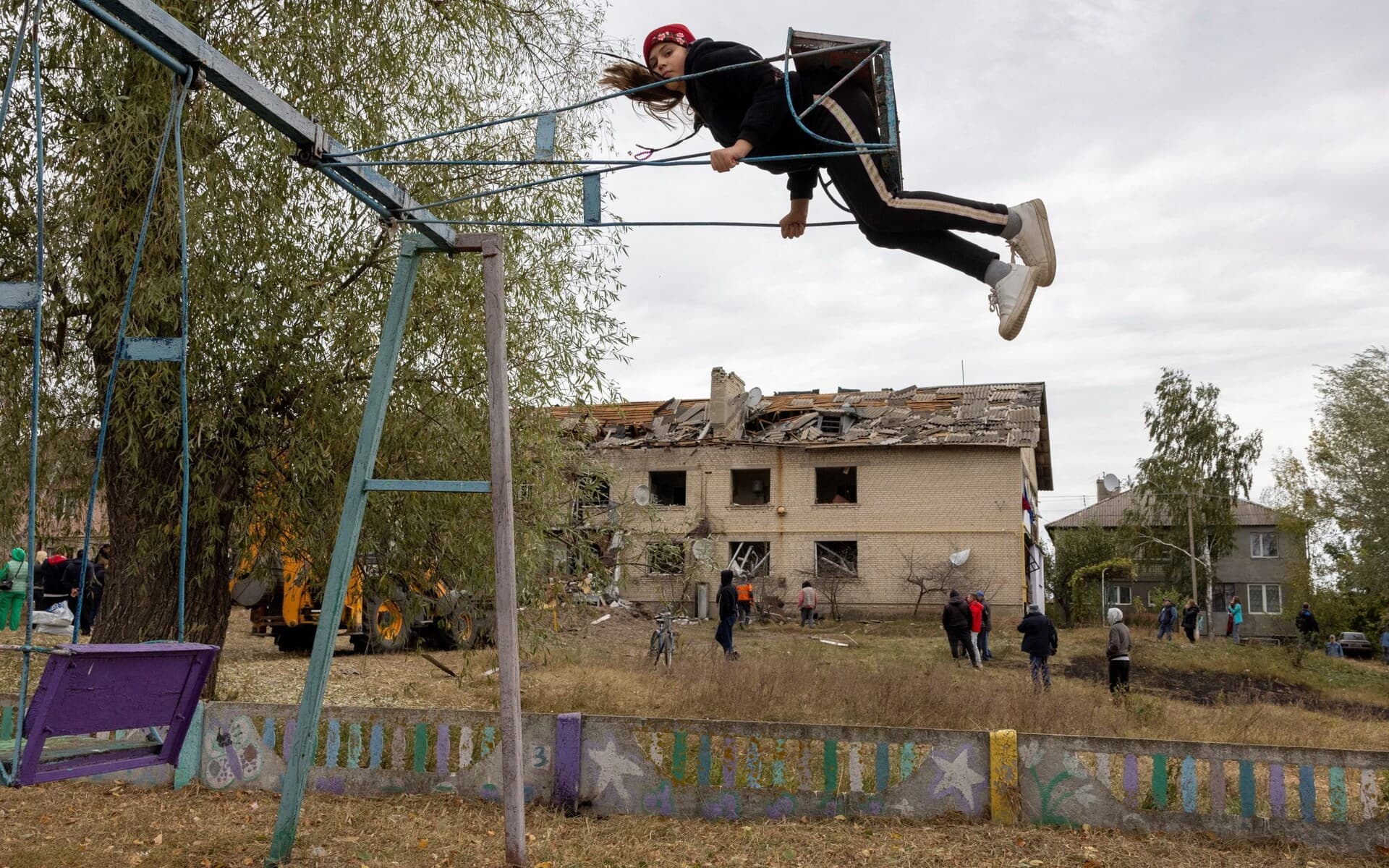 A child sits on a swing near an apartment building damaged by the impact of a Russian S-300 missile near Kharkiv