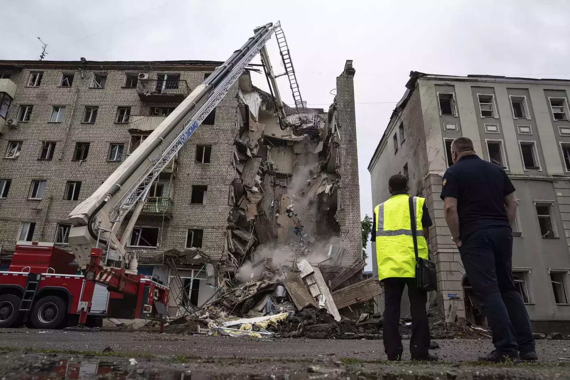 Rescue workers put out the fire of a destroyed car after a Russian attack in a residential neighborhood in downtown Kharkiv