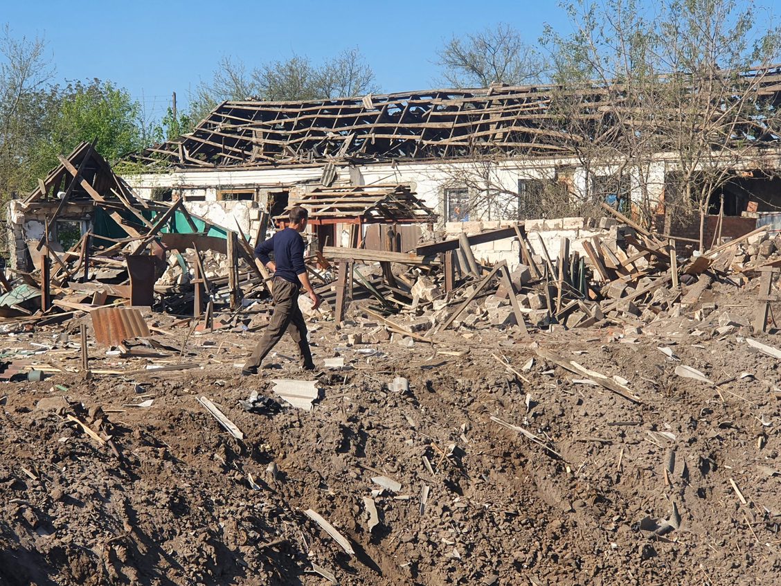 A man walks between a bomb crater and the ruins of a row of houses that the explosion destroyed in Malotaranivka