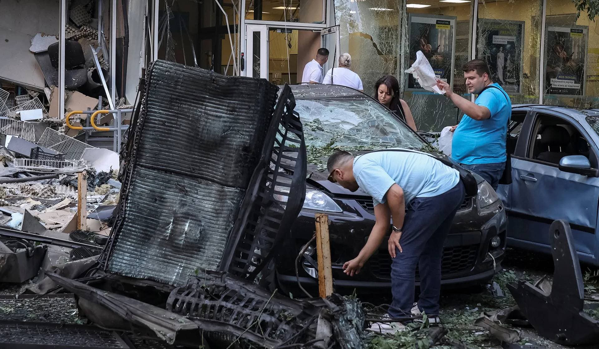 Residents inspect a damaged car at the site of the Russian drone strike in Odesa