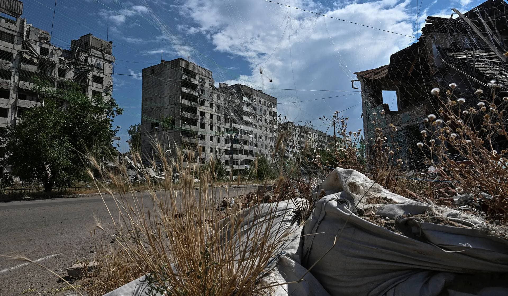 A residential building damaged by Russian military strikes and anti-drone nets installed over a street in the frontline town Orikhiv