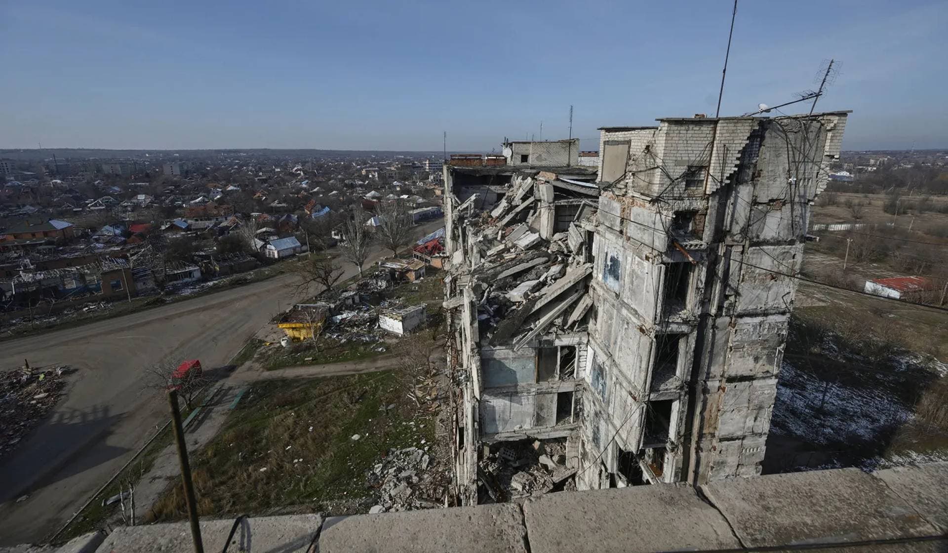 Ukrainian national flags flutter in front of a heavily damaged apartment building in Orikhiv